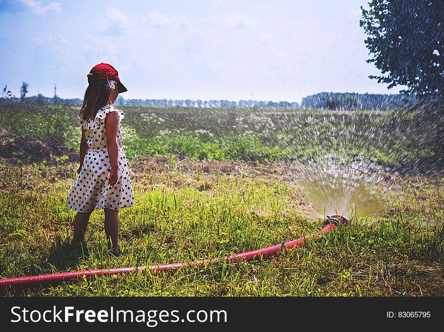 Girl on Green Grass Near Red Hose While Pumping Water during Daytime