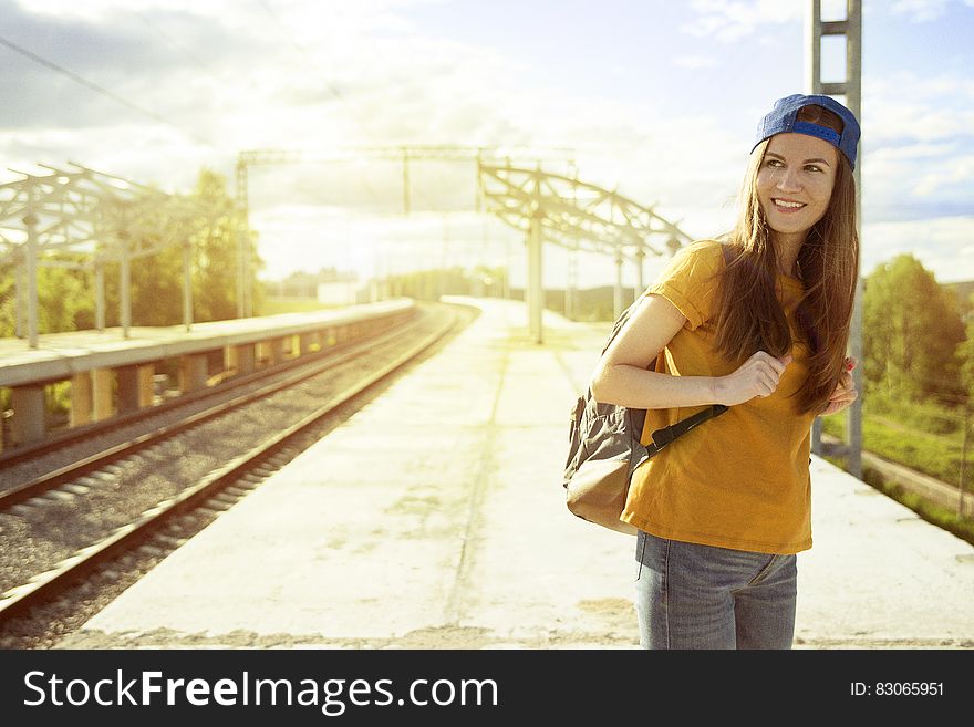 Smiling Woman In Orange T Shirt And Blue Snap Back Cap Carrying Backpack