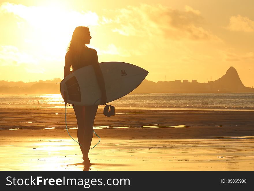 Woman Holding Surf Board Standing on Shoreline during Sunset