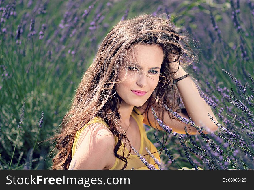 Women&x27;s Yellow Tank Top Holding Her Brown Curly Hair While Sitting On A Purple Flower