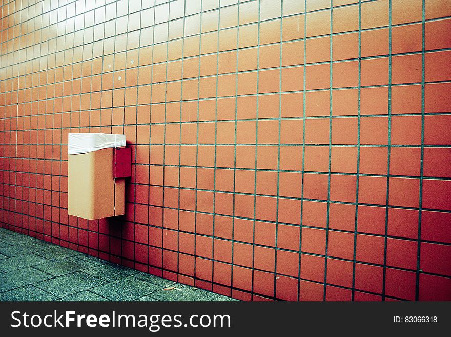 Trash can mounted on wall with orange tiles by floor with green tiles. Trash can mounted on wall with orange tiles by floor with green tiles.