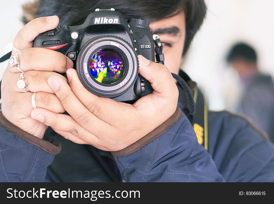 Young man in blue jacket taking a picture with a Nikon single lens reflex digital camera. He is composing the picture and focusing while viewing the scene through the eye piece. Young man in blue jacket taking a picture with a Nikon single lens reflex digital camera. He is composing the picture and focusing while viewing the scene through the eye piece.