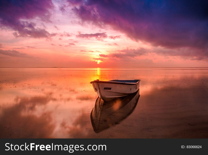 Small boat anchored in a bay on a tranquil sea colored by a magical sunrise of orange, yellow, purple and brown. Small boat anchored in a bay on a tranquil sea colored by a magical sunrise of orange, yellow, purple and brown.
