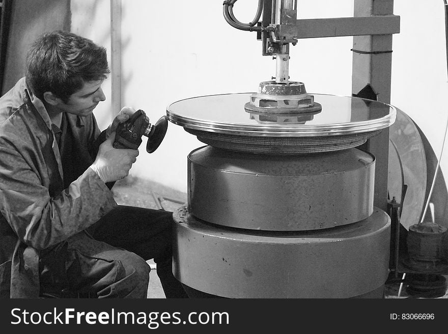 A black and white photo of a craftsman polishing a round metal glass frame. A black and white photo of a craftsman polishing a round metal glass frame.