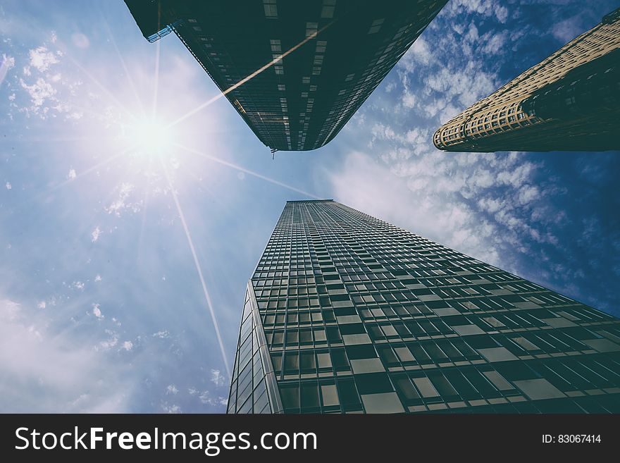 View looking up to top of three tall skyscrapers in city with cloudscape and sun flare. View looking up to top of three tall skyscrapers in city with cloudscape and sun flare.