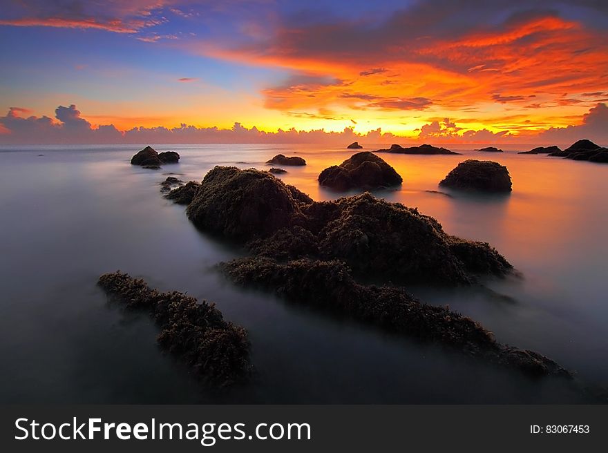 A sunset on the seashore with rocks rising from the water. A sunset on the seashore with rocks rising from the water.