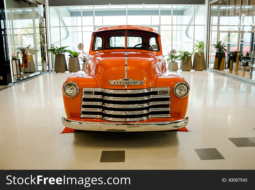 Orange colored Chevrolet sedan (saloon car) from 1950's in pristine condition with attractive chrome grill and headlights, pride of the garage and in the center of the showroom.