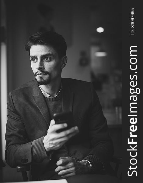 A black and white photo of a young businessman with a far off look holding smartphone. A black and white photo of a young businessman with a far off look holding smartphone.