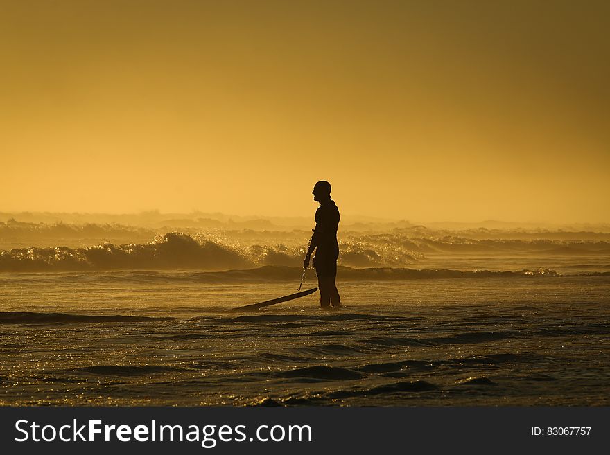 Man Standing on Seashore While Holding His Surfing Board during Sunset