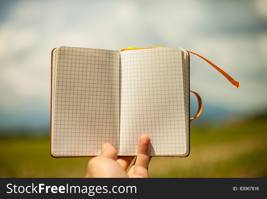 A close up of a hand holding an open blank notepad.