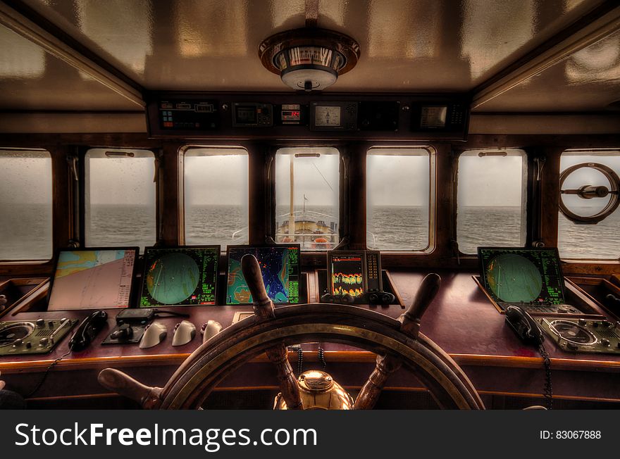 View from the wheelhouse of a older style ship across quiet sea to the horizon in darkening light with radar, navigation aids, telephone and wheel.