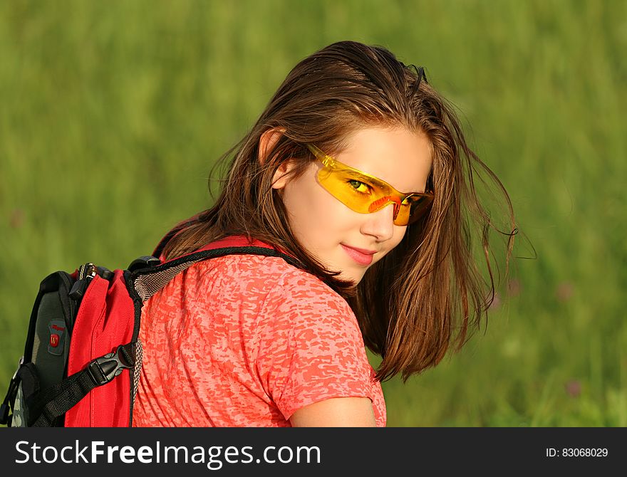 Woman in Red Shirt Wearing Backpack Surrounded by Green Grass Field