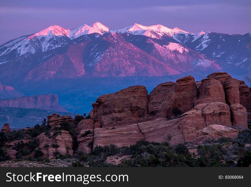 Green Trees and Rock Formation Overlooking Snow Coated Mountain Ranges at Daytime