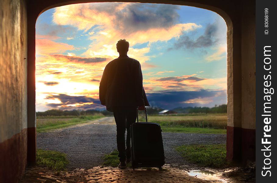 Man Pulling Luggage Walking Near Gray Concrete Road during Sunset