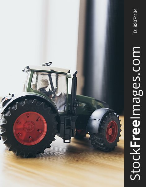 Black and Green Farm Tractor Toy on Brown Wooden Table Beside Window