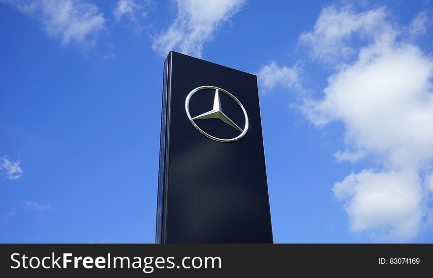A Mercedes-Benz sign on a stand against the blue skies. A Mercedes-Benz sign on a stand against the blue skies.