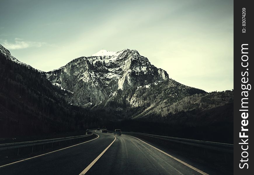 Asphalt Road With Running Vehicle Infront Of Mountain Under Gray Sky