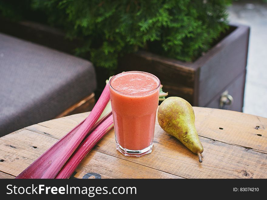 A fruit smoothie with rhubarb stalks and pear next to it.