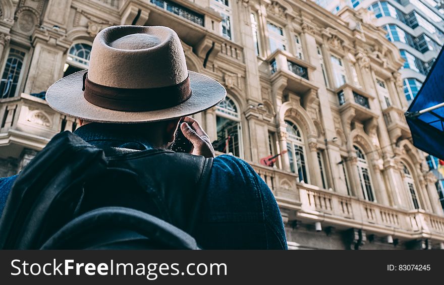 Man in Beige Hat Taking Picture on Beqige Conrete Architectural Building