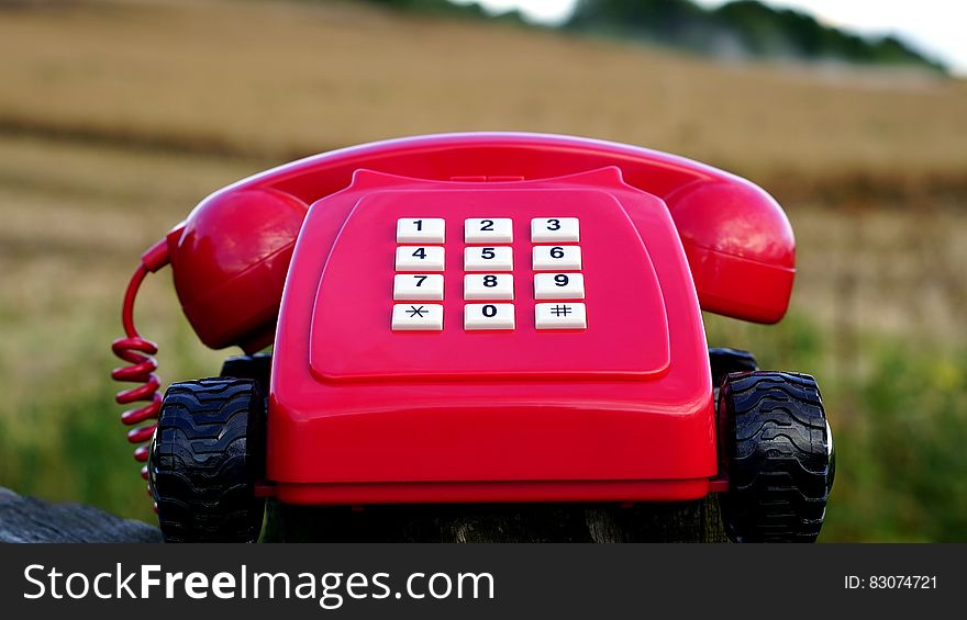 Red Rotary Phone With Black Wheels Near Brown Grasses During Day Time