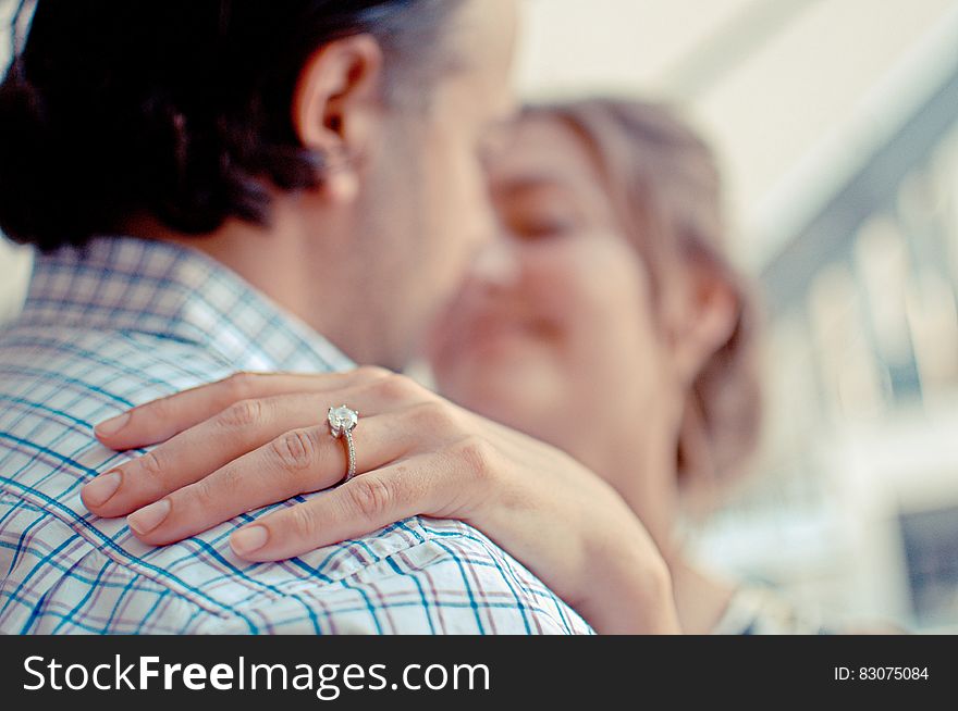 Closeup of couple having a hug but with selective focus on a diamond ring on the woman's finger and their faces are blurred.