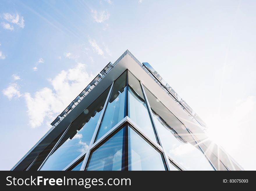 Corner of modern glass and concrete building with narrow elegant frames appearing to converge towards the high point, pale blue sky with thin cloud. Corner of modern glass and concrete building with narrow elegant frames appearing to converge towards the high point, pale blue sky with thin cloud.