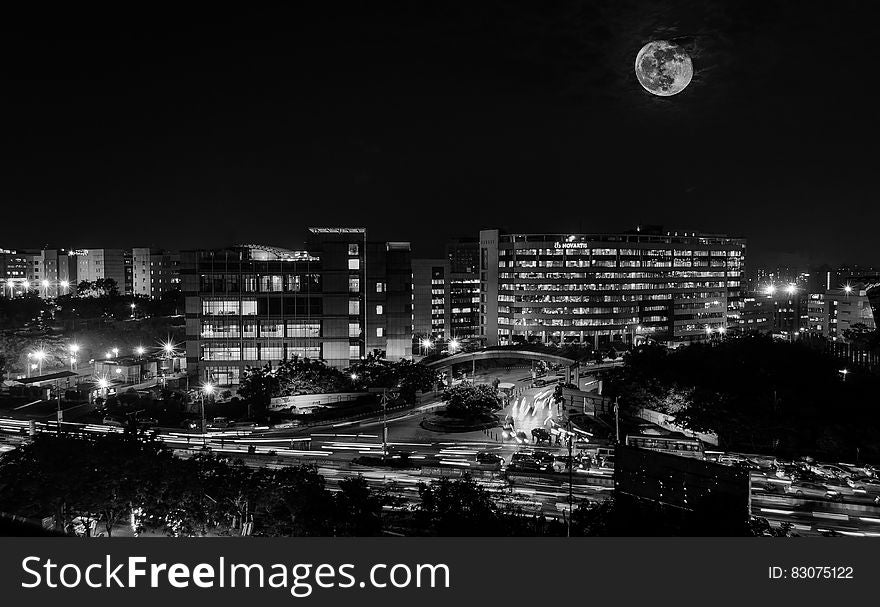 A black and white photo of full moon above city.