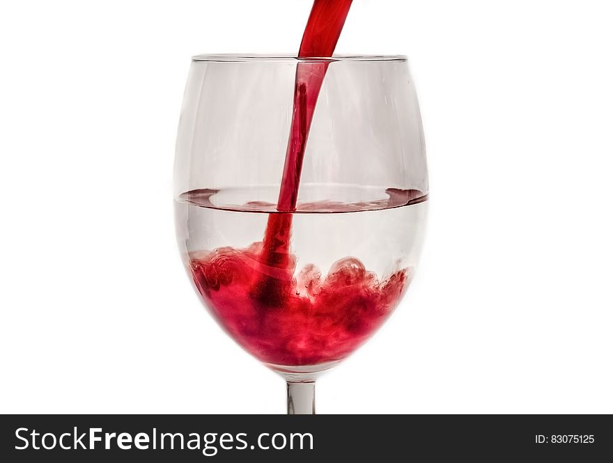 Pouring red soda into a glass with transparent liquid inside.