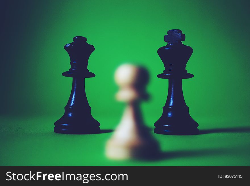 Close up of black queen and king chess pieces with white pawn on green background. Close up of black queen and king chess pieces with white pawn on green background.