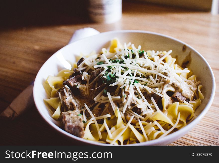 Bowl of pasta noodles with meat and shredded vegetables on wooden table. Bowl of pasta noodles with meat and shredded vegetables on wooden table.