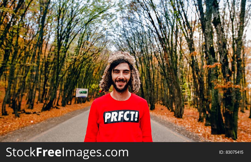 Man wearing red sweatshirt and fur hat standing in country road lined with autumn trees on sunny day. Man wearing red sweatshirt and fur hat standing in country road lined with autumn trees on sunny day.