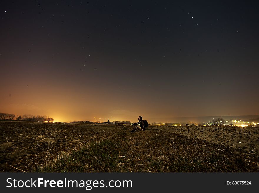Man sitting on hillside over town illuminated at night. Man sitting on hillside over town illuminated at night.