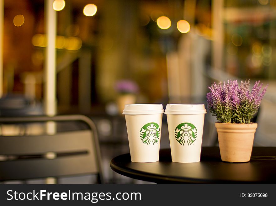 Starbucks coffee cups on patio table with potted plant.