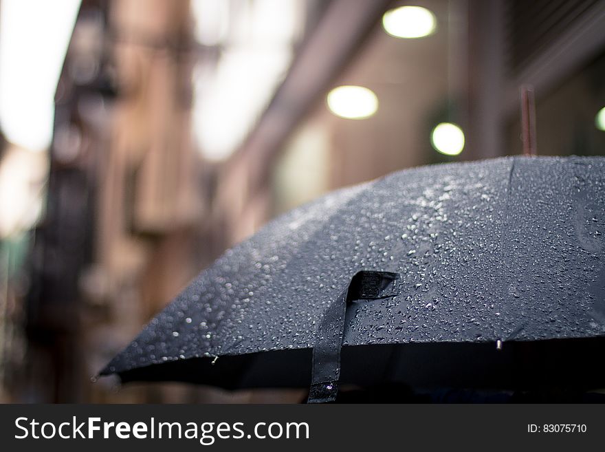 Closeup of umbrella in the rain with selective focus on rain drops, blurred urban background.