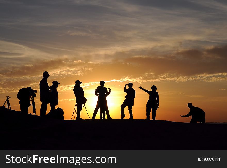 A view of a hill with the silhouettes of people filming and photographing the sunset. A view of a hill with the silhouettes of people filming and photographing the sunset.