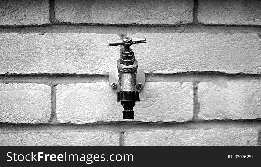 Grayscale of Metal Faucet on Wall Brick