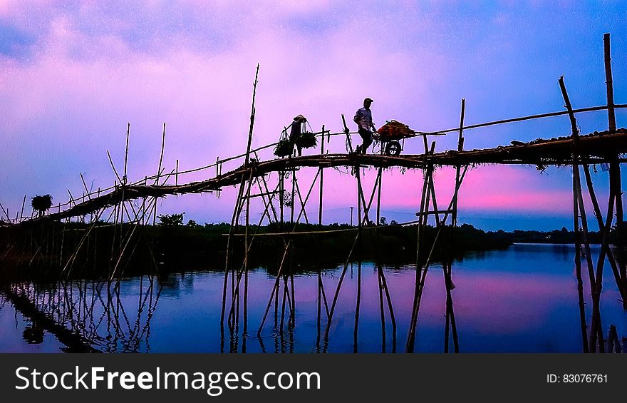 3 Person Walking on Bridge Under Cloudy Sky during Sunrise