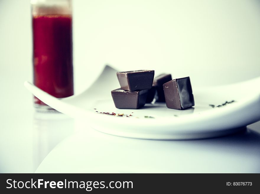 Chocolate cubes on a white plate and red juice in the background. Chocolate cubes on a white plate and red juice in the background.