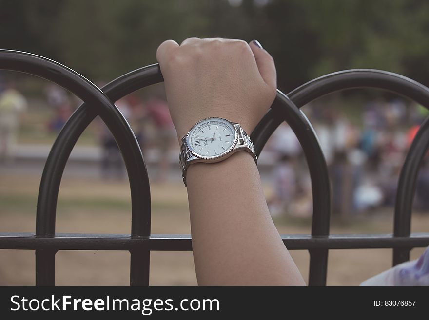 Closeup of woman's hand with watch on her wrist holding painted black metal railings. Closeup of woman's hand with watch on her wrist holding painted black metal railings