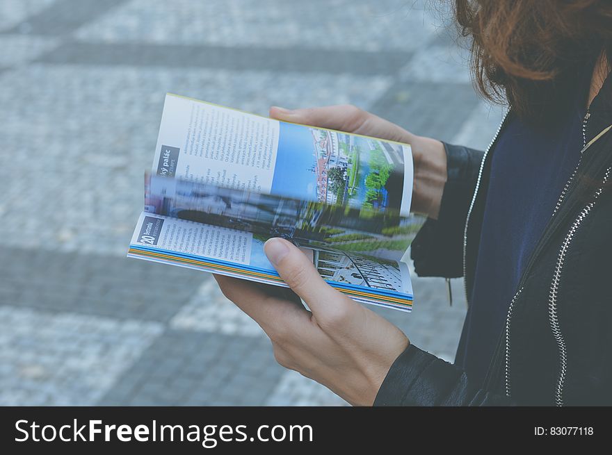 Woman in Black Zipped Jacket Hoding White and Blue Book