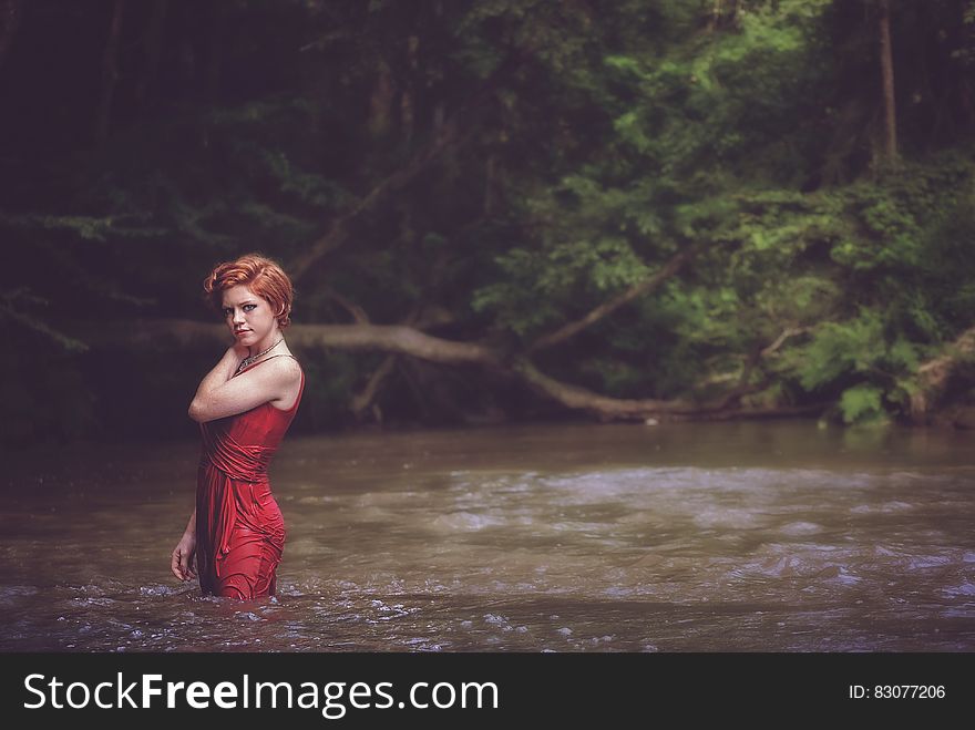 Woman In Red String Spaghetti Strap Dress On Body Of Water Near Forest