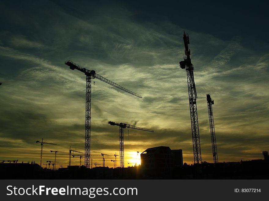 A construction site at sunset with tower cranes.