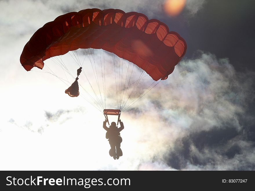 A silhouette of a person parachuting in cloudy sky.