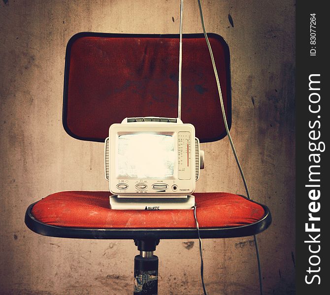 An old fashioned model of a TV on a red chair. An old fashioned model of a TV on a red chair.