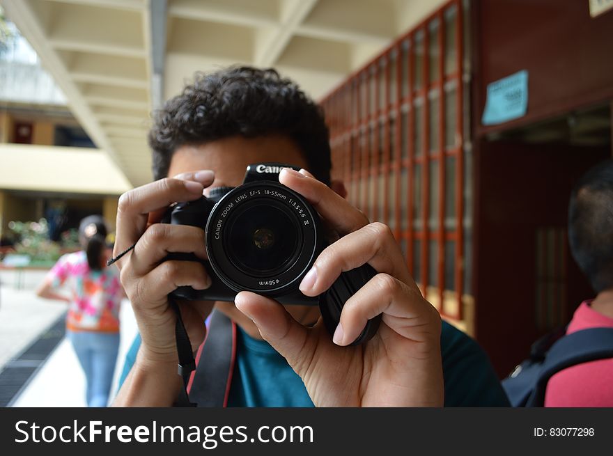 Closeup of young man with dark curly hair holding Canon digital single lens reflex camera while looking through viewfinder, urban background. Closeup of young man with dark curly hair holding Canon digital single lens reflex camera while looking through viewfinder, urban background.