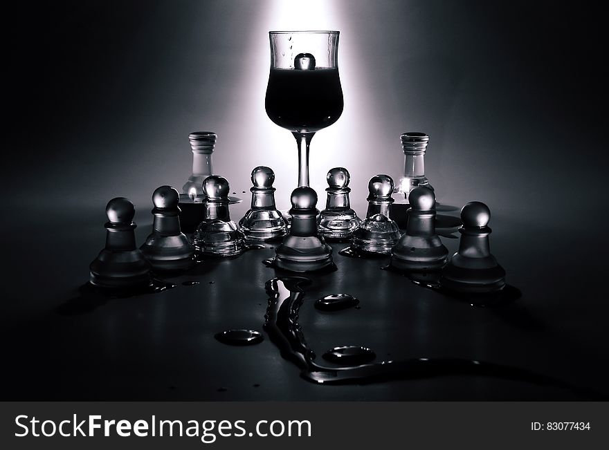 A wine glass standing in the middle of glass chess pieces. A wine glass standing in the middle of glass chess pieces.