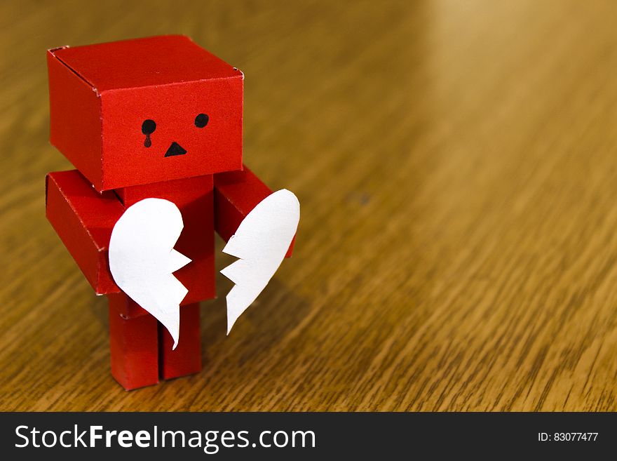 Crying red cardboard model holding broken love heart on wooden background with copy space. Crying red cardboard model holding broken love heart on wooden background with copy space.