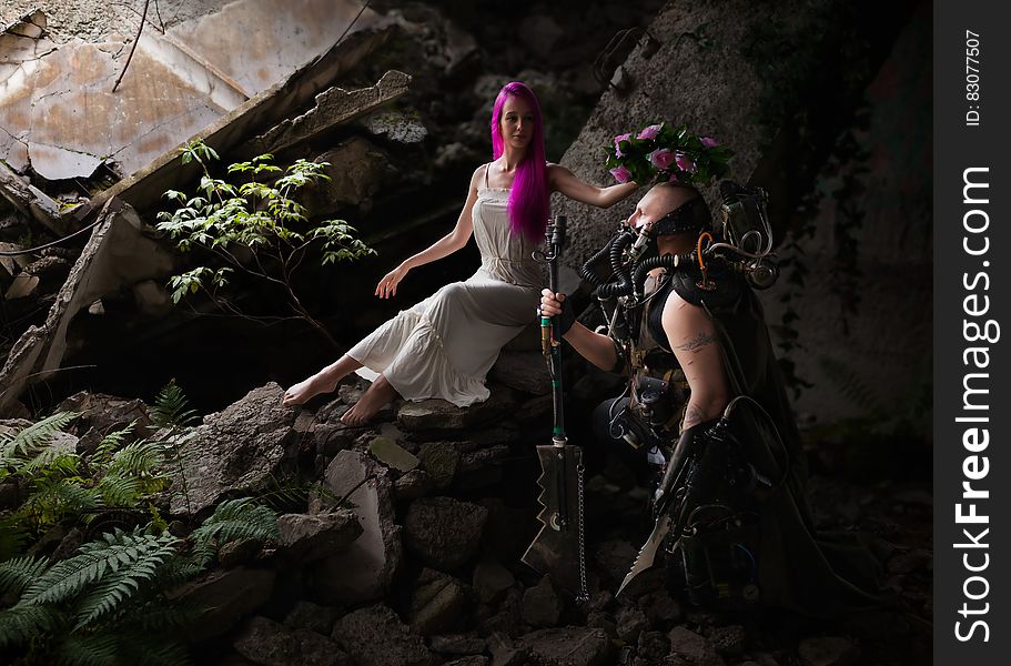 Woman With Purple Hair Wearing White Sleeveless Dress Sitting On The Rocks Holding Pink Floral Headband