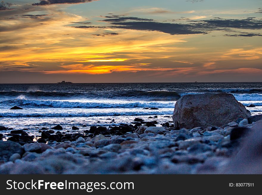 Scenic view of waves breaking on rocky beach at sunset. Scenic view of waves breaking on rocky beach at sunset.