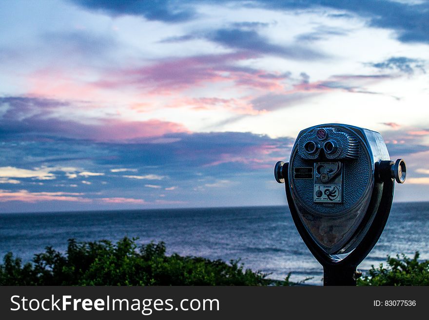 Gray And Black Tower Viewer Near Green Grass Field And Beach Under Blue White And Gray Clouds